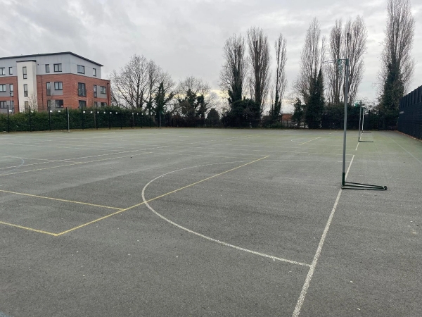Love Locations open playground shoot location Reading RG30: Outdoor asphalt sports surface flanked by tall trees and school boundaries, perfect for lifestyle photography and athletic drills.