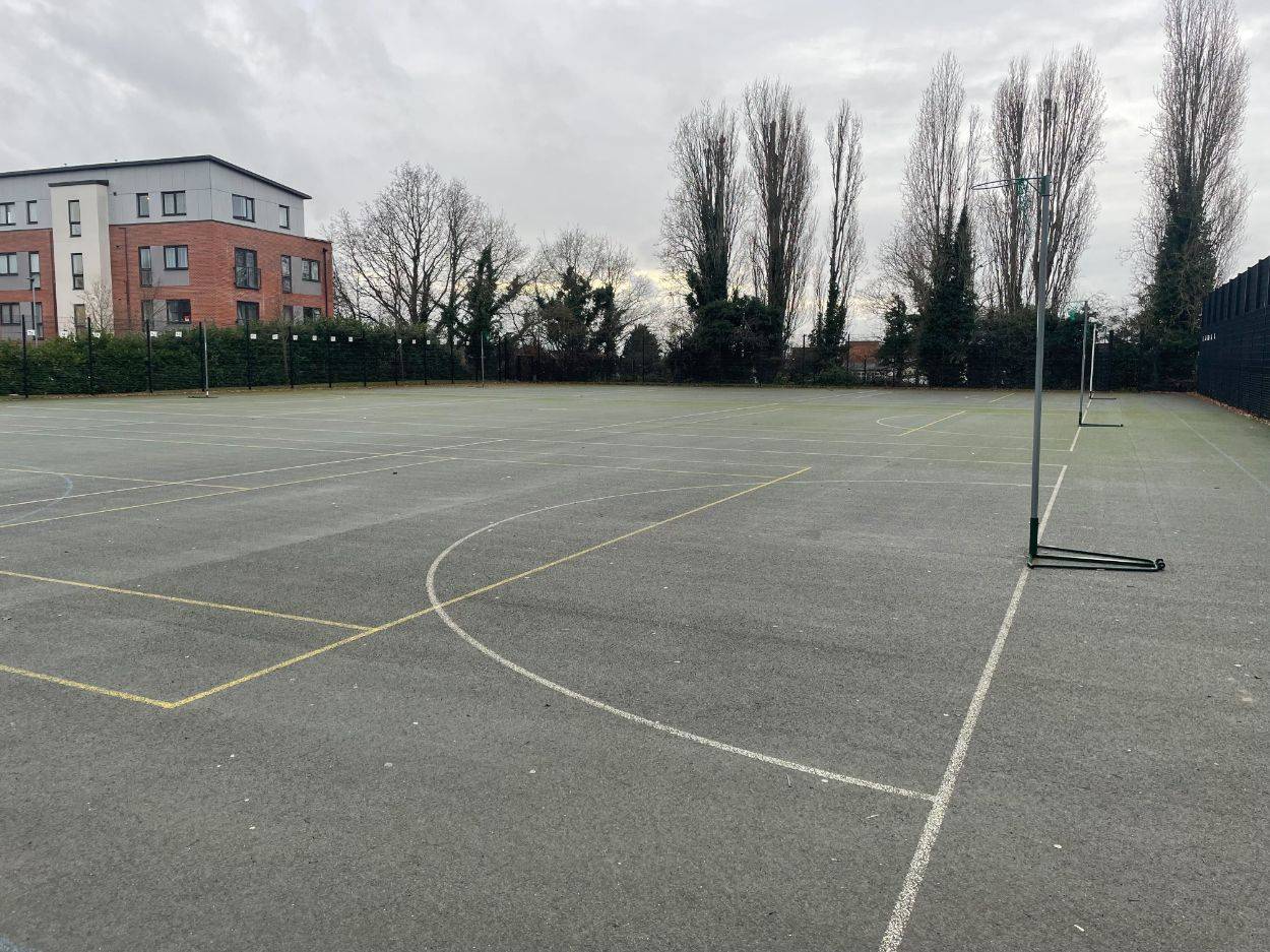 Love Locations open playground shoot location Reading RG30: Outdoor asphalt sports surface flanked by tall trees and school boundaries, perfect for lifestyle photography and athletic drills.