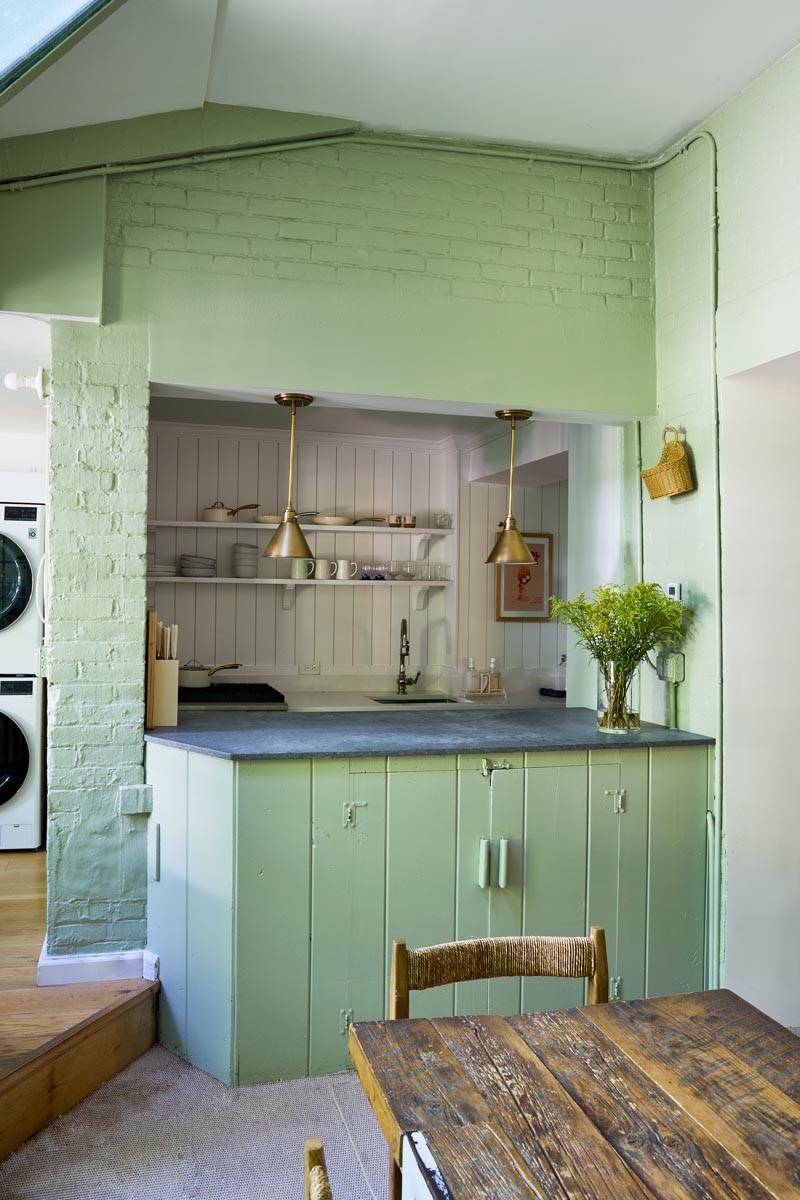 Sage green open-plan kitchen shoot space in a Manhattan NY 10014 location home through Love Locations, featuring soft green cabinetry, a breakfast bar cutout, and beadboard wall panelling.