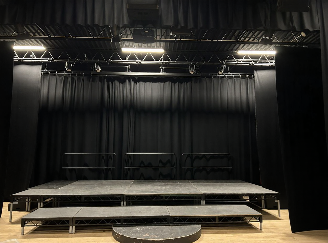 Black box theater stage setup with black curtain backdrop and tiered performance riser in Kent via Love Locations.