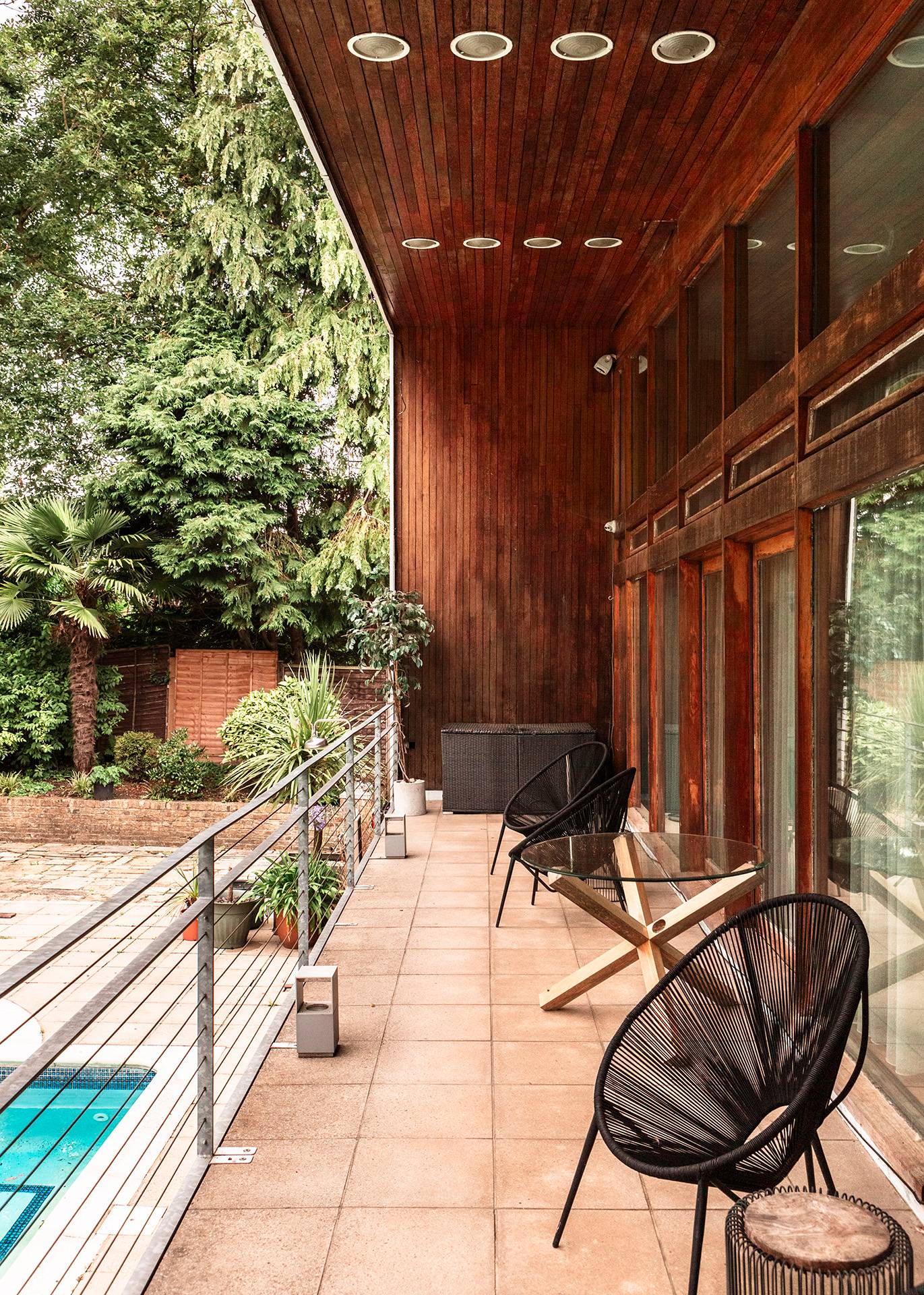 Elevated wooden balcony lounge area overlooking the swimming pool and private woodland garden in Bromley, Love Locations.