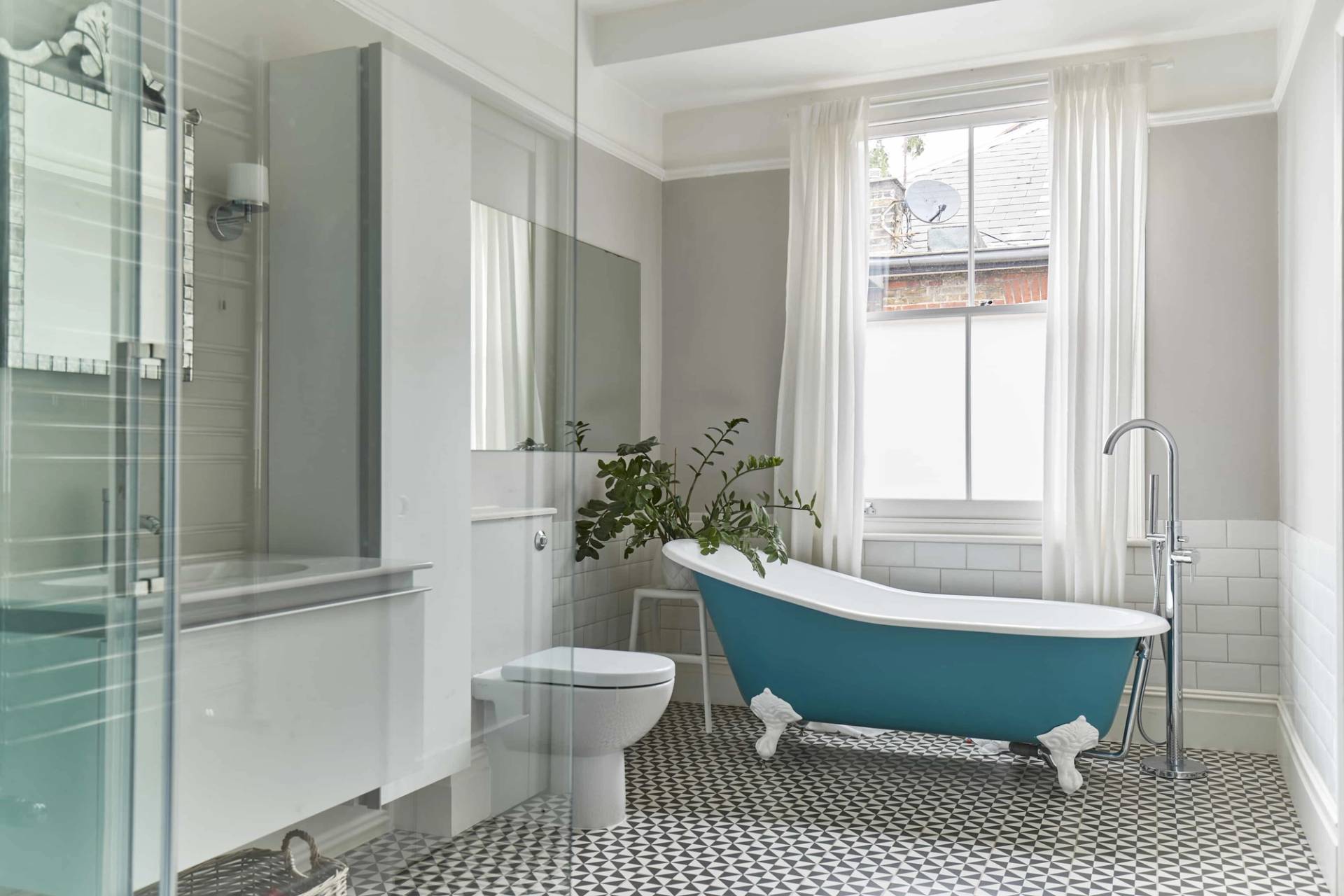 Period bathroom suite in Ealing Common, W3 featuring a teal roll-top bath, glass shower screen, and black and white patterned tile flooring, Love Locations.