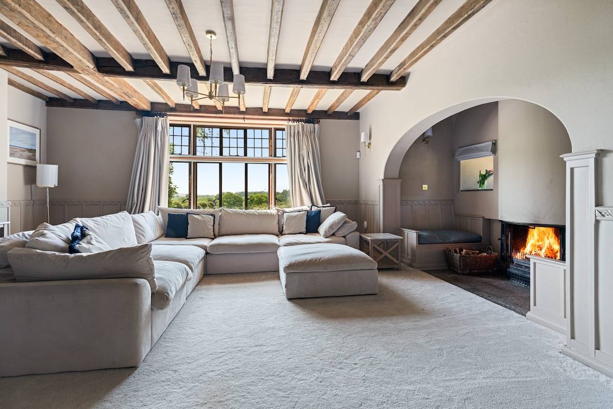 Family TV lounge room with a grey corner sofa, plush carpet, and exposed ceiling timber beams, Love Locations RH13.