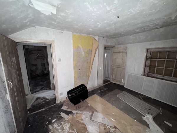 Spooky interior scene with a vintage black suitcase sitting on a plaster-covered floor next to an open doorway, Love Locations NG9.