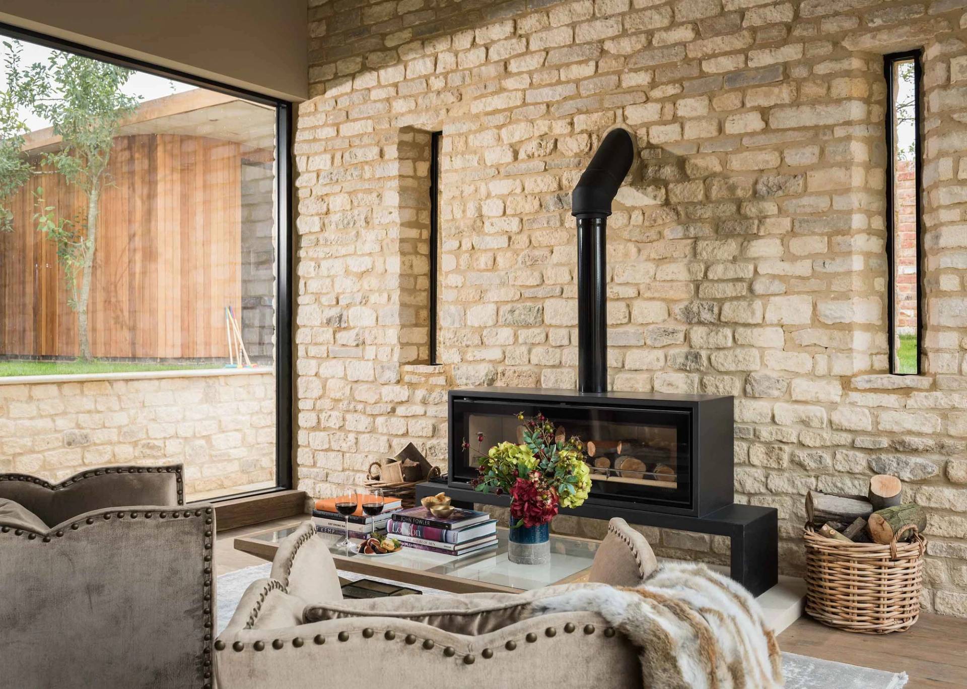 Cozy stone-walled seating area with a modern black log burner stove inside a Cotswold location home via Love Locations.