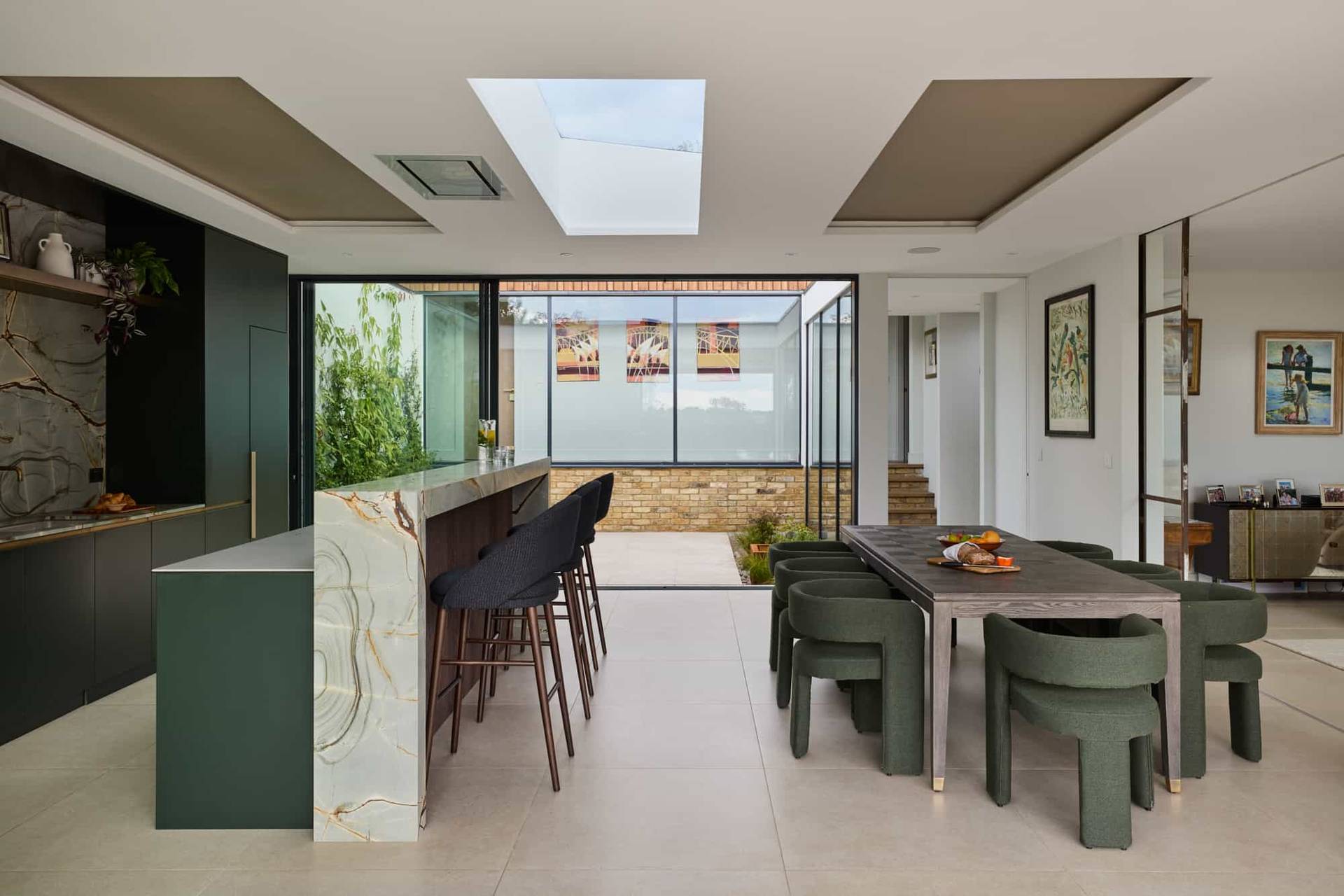 Sleek kitchen island breakfast bar with dark stools and marble waterfall countertops opening to a courtyard garden, ideal for culinary ads, Love Locations.