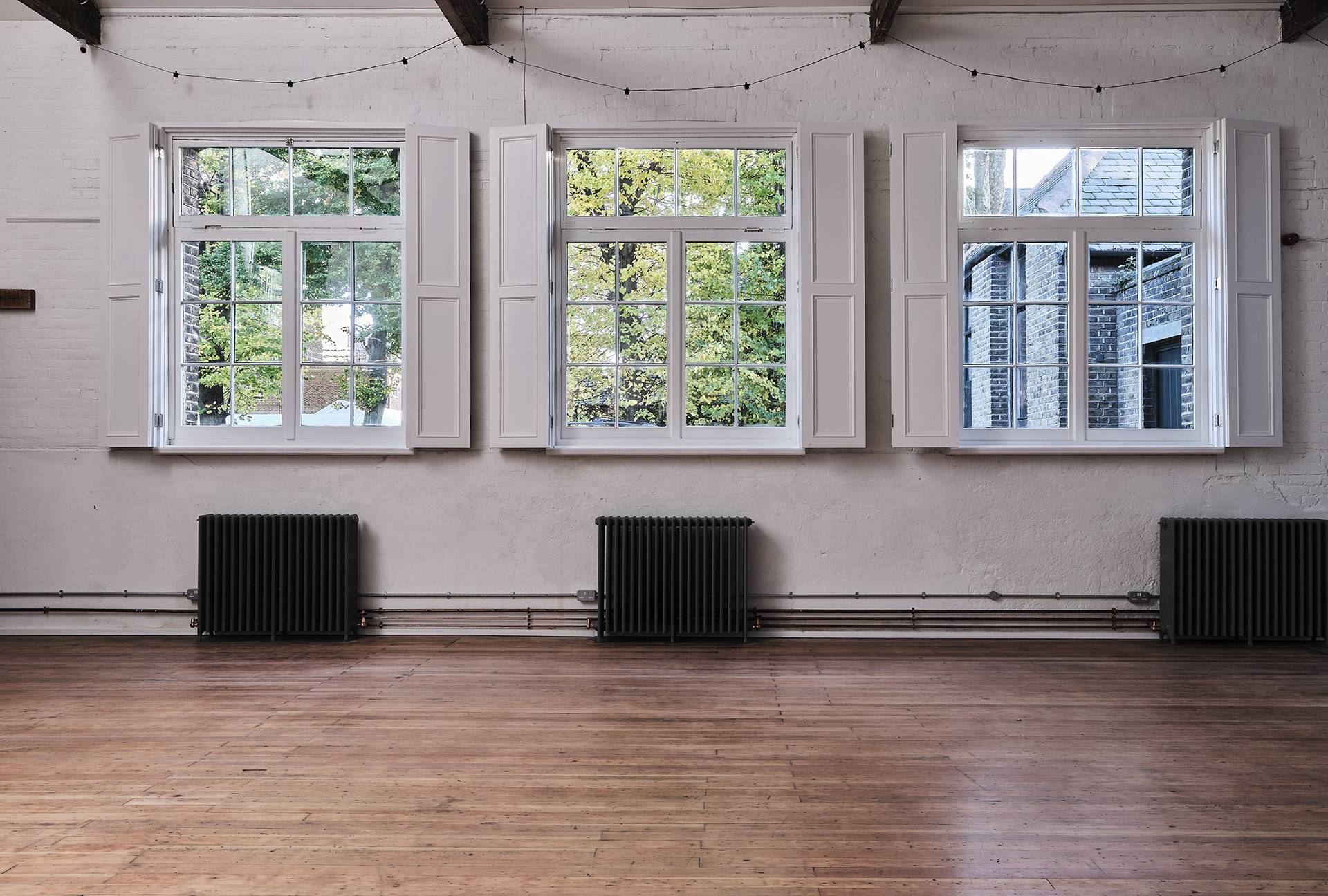 Detail shot of multi-pane windows with white shutters and cast iron radiators set in a white hall room, Love Locations.