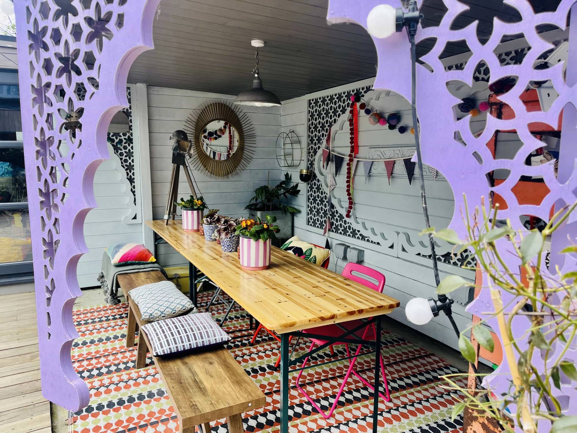 Outdoor covered dining terrace with a long wooden table, benches, and purple carved veranda trim, Love Locations Catford.