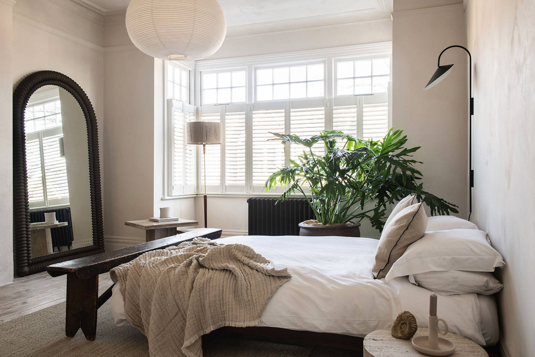 Minimalist bedroom corner with micro-cement walls, arched floor mirror, and dark wood bench, perfect for e-commerce fashion lookbooks, Love Locations.