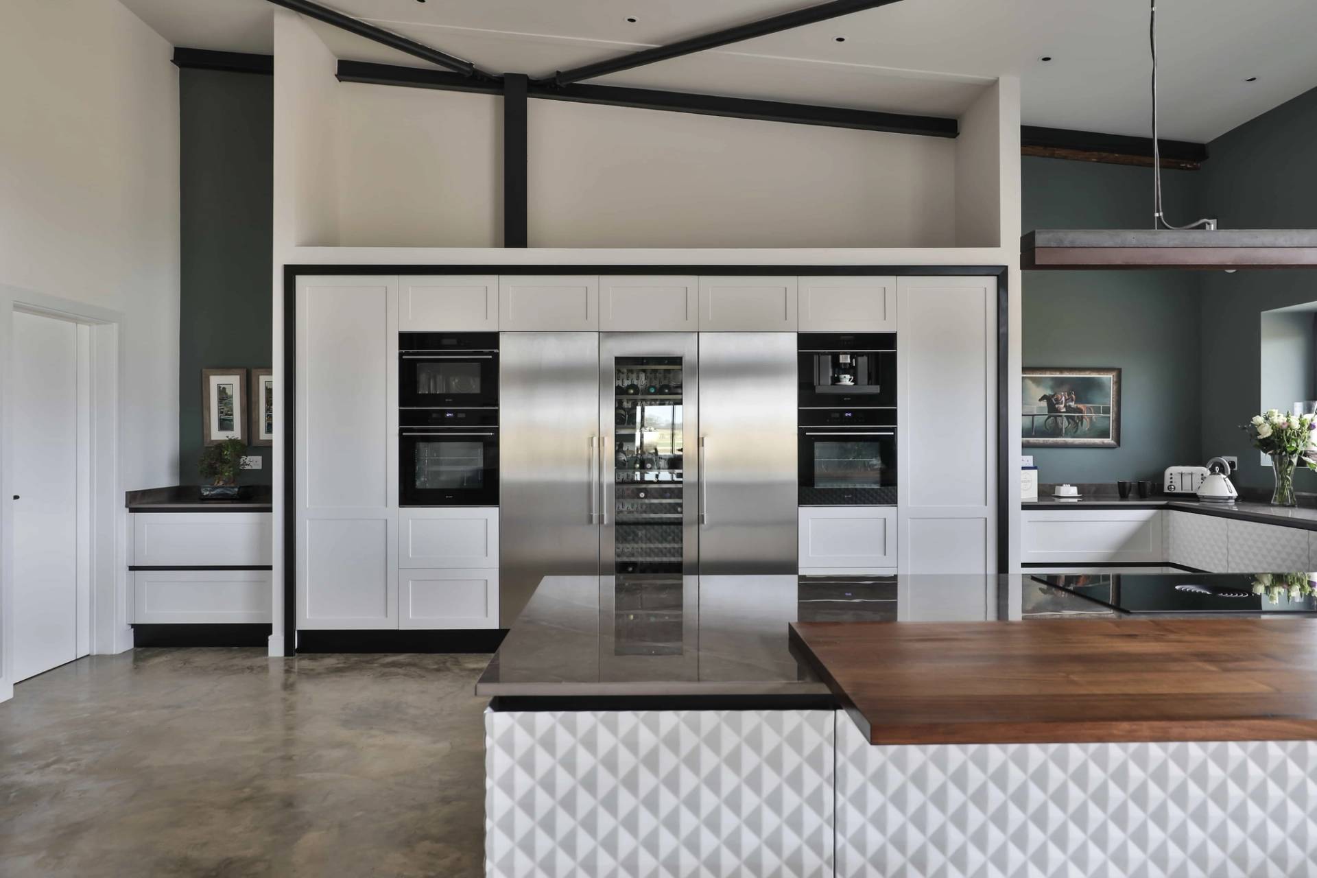 Sleek kitchen bank wall with integrated stainless steel appliances, double ovens, and wooden prep counters, Love Locations CV23.