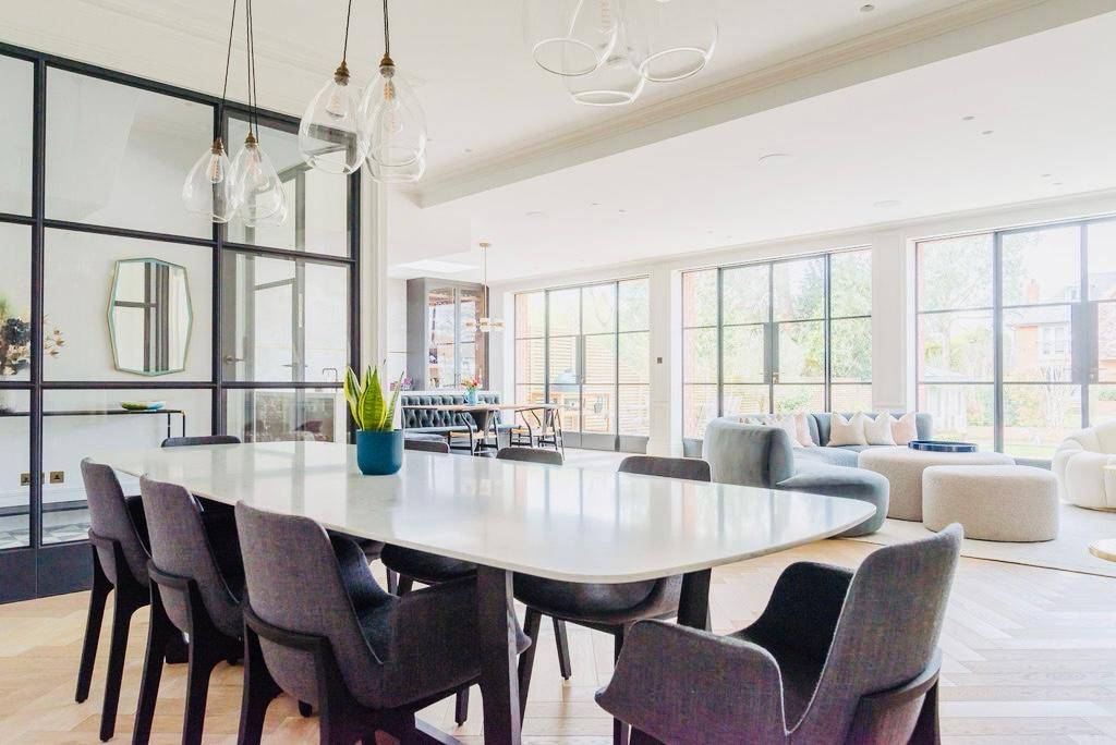 Formal dining area set with a modern oval table and grey upholstered chairs under pendant lights, Love Locations TW11.