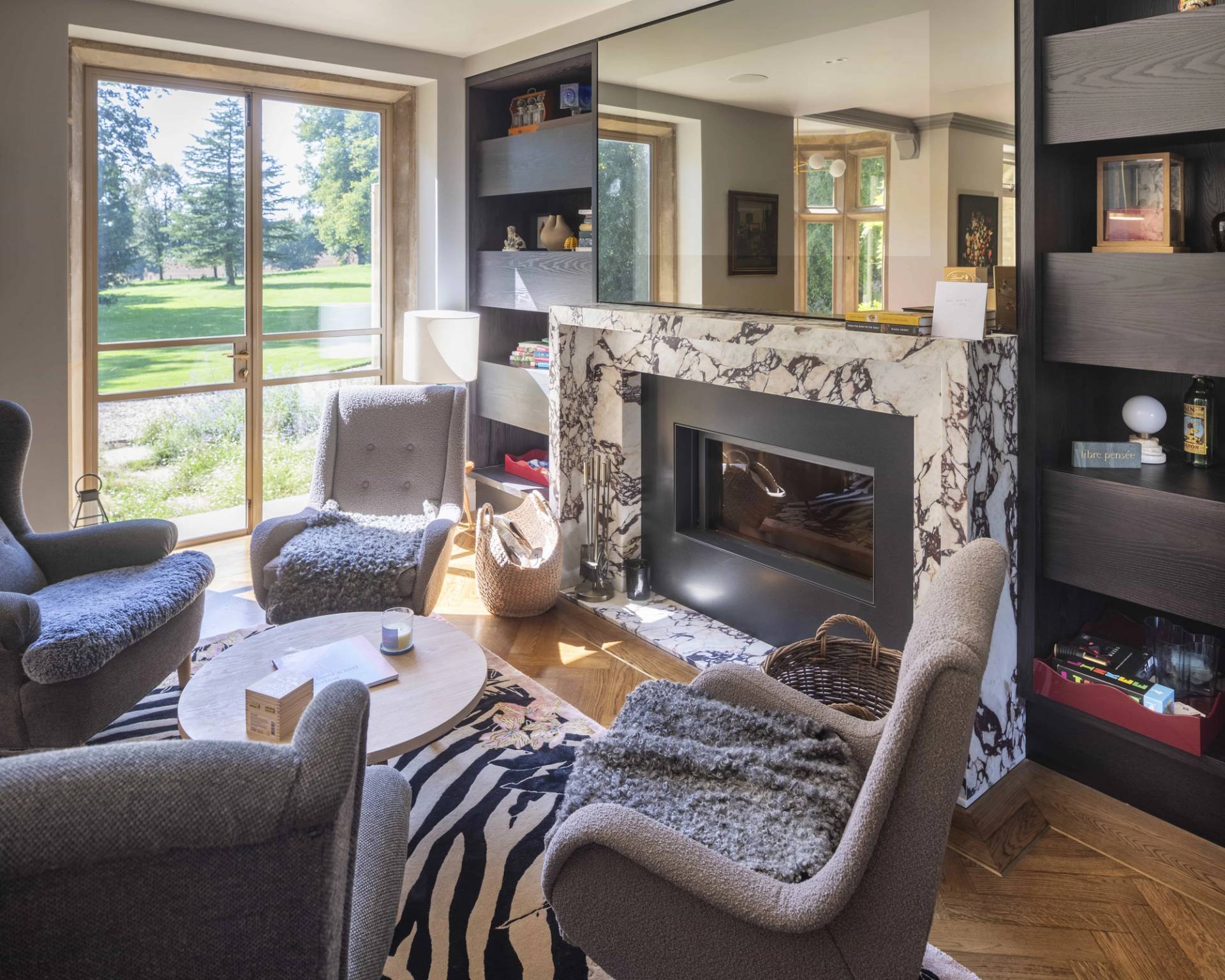 Close-up view of a marble fireplace surround set beside dark built-in bookshelves and grey armchairs, Love Locations OX7.