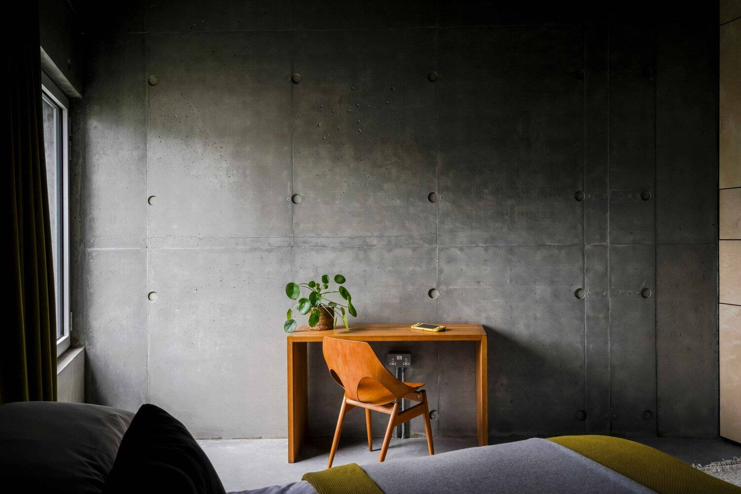 Minimalist study desk setup set against a raw board-marked concrete wall with an orange desk chair, Love Locations BN7.