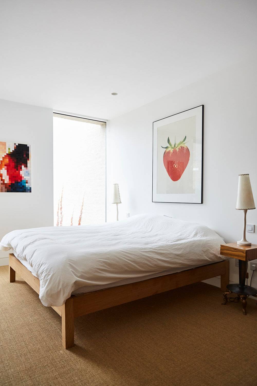 Bright minimalist bedroom with crisp white walls, natural timber bed frame, and strawberry wall art piece, perfect for contemporary domestic lifestyle shoots, Love Locations.