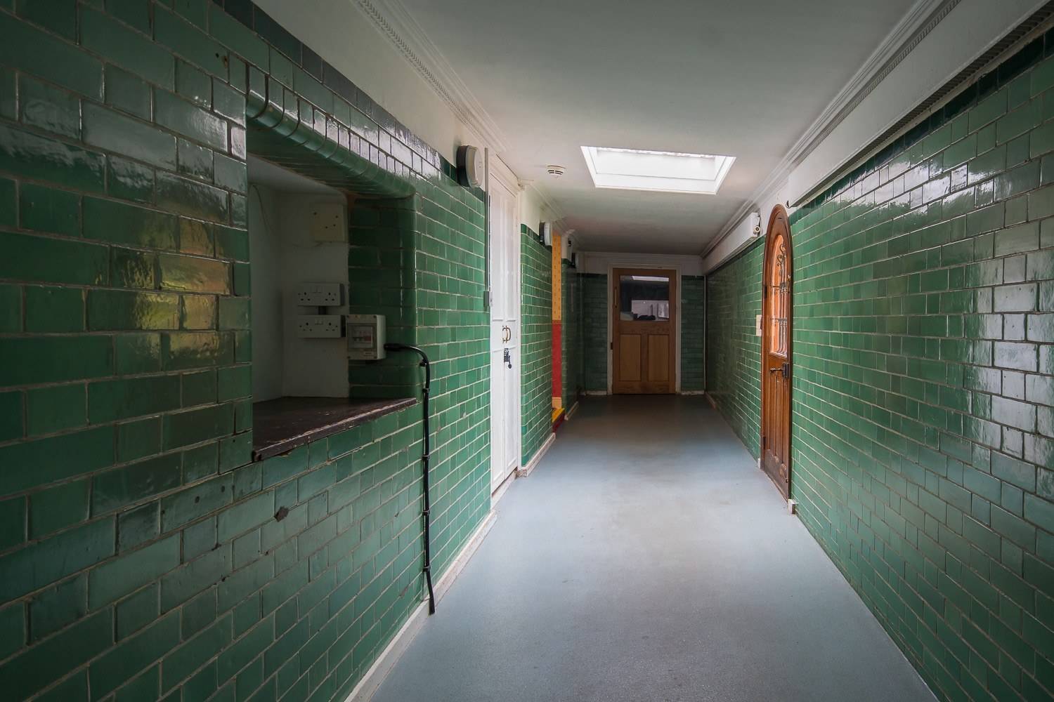 Institutional service corridor film location featuring green glazed wall tiles and timber doors via Love Locations.