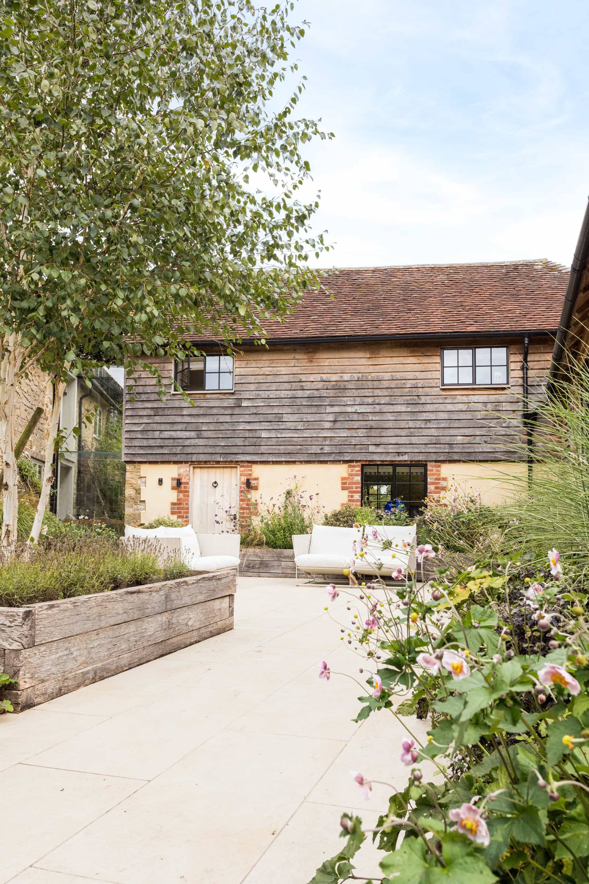 Paved outdoor courtyard patio set behind a converted timber weatherboard barn, Love Locations GU28.