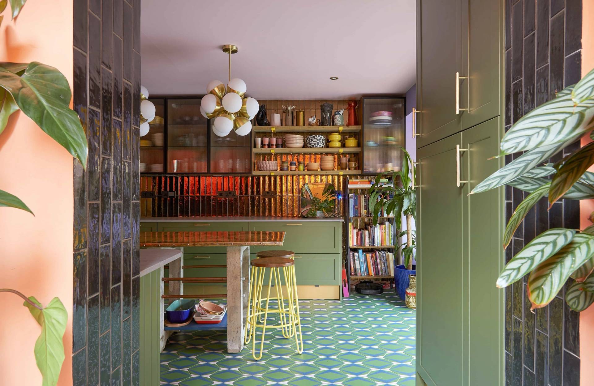 Olive green kitchen suite with open display shelving filled with ceramics and books set under a pink ceiling, Love Locations SE6.