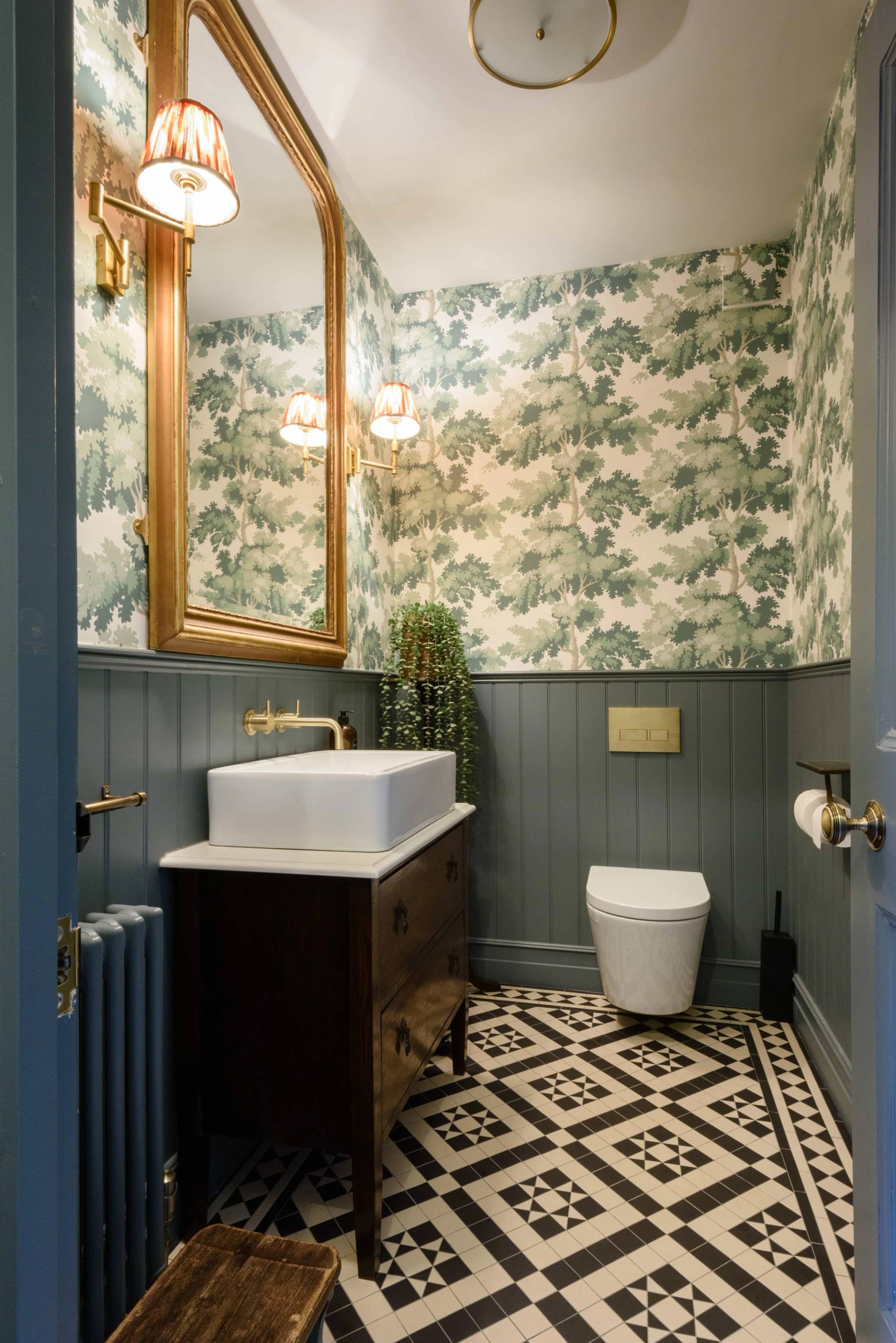 Powder room featuring botanical wallpaper, forest green wall panelling, dark vanity, and geometric floor tiles, Love Locations TW11.