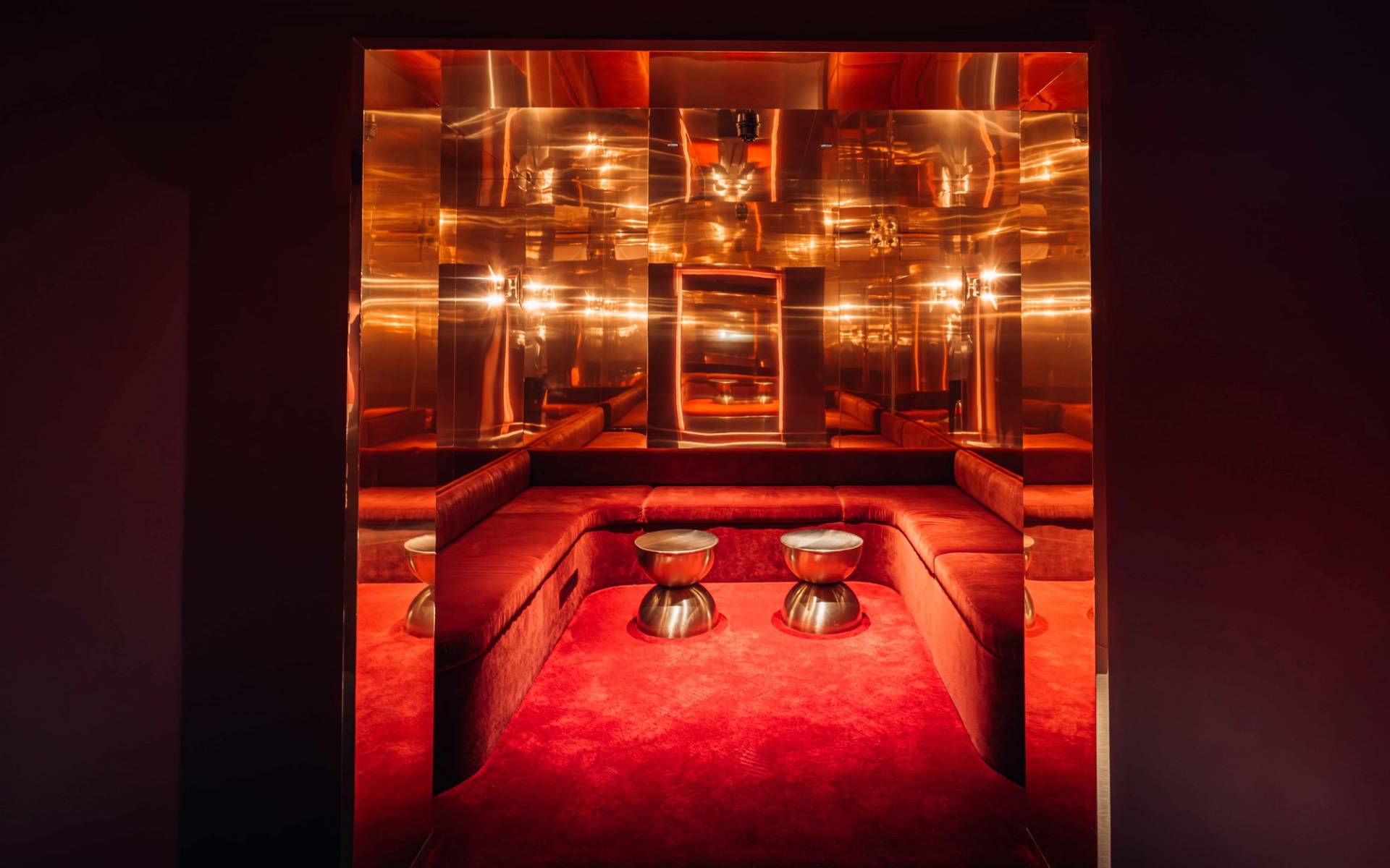 Mirrored geometric booth alcove with plush red velvet banquette seating and chrome drum tables inside Plonkers Parlour in Brentford TW8 through Love Locations.