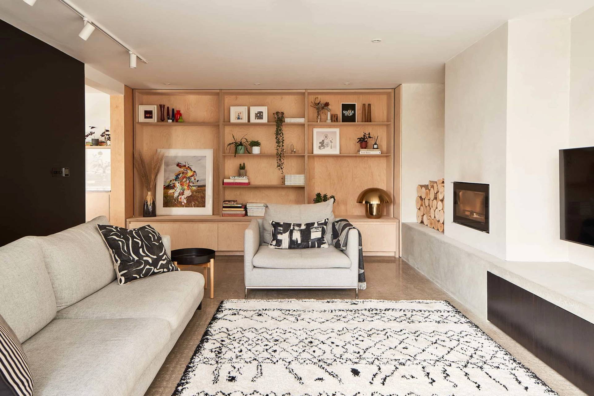 Modern barn conversion lounge shoot location in Suffolk, IP30 featuring light wood shelving, neutral sofa, fireplace, and patterned rug via Love Locations.