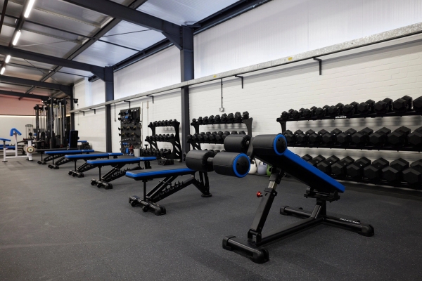 Professional strength training benches and free weight racks set against a white brick wall in a commercial gym, Love Locations SO23.