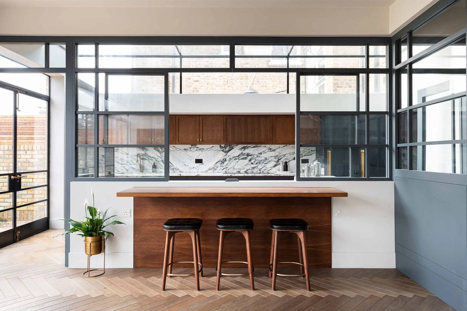 Dark wood kitchen island counter set before a crittall window partition wall, Love Locations.