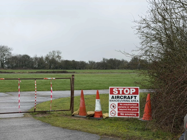 Airfield access track featuring red-and-white safety bollards and restricted area signage, perfect for unit base parking and crew logistics, Love Locations NN17.