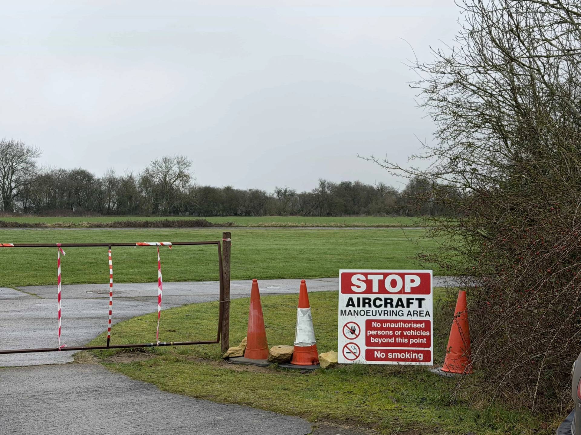 Airfield access track featuring red-and-white safety bollards and restricted area signage, perfect for unit base parking and crew logistics, Love Locations NN17.