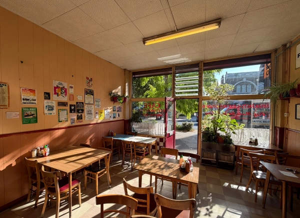 Retro London greasy spoon cafe dining area with wooden tables, chairs, yellow walls, and large shopfront windows in Tulse Hill, Love Locations SE27.
