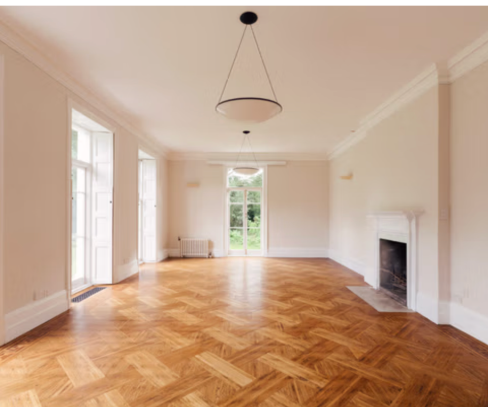 Elegant drawing room at Bell House featuring decorative wall panelling, an ornate arched leaded window, a white sofa, classic chandelier, and original Georgian architectural details.