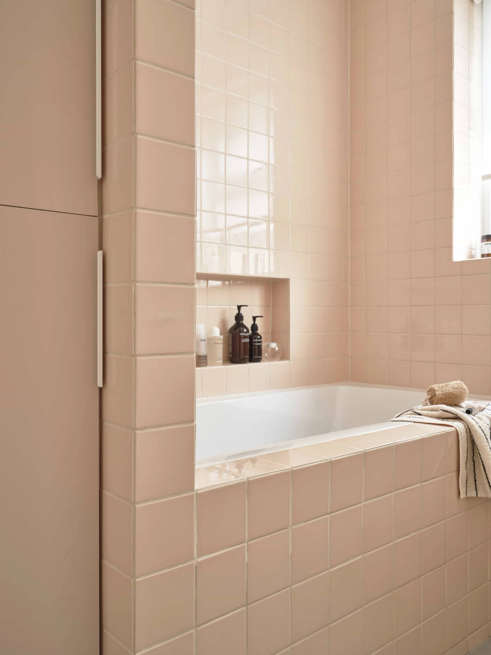 Monochrome blush-pink tiled bathroom with built-in shower niche and white porcelain tub, Love Locations E4.