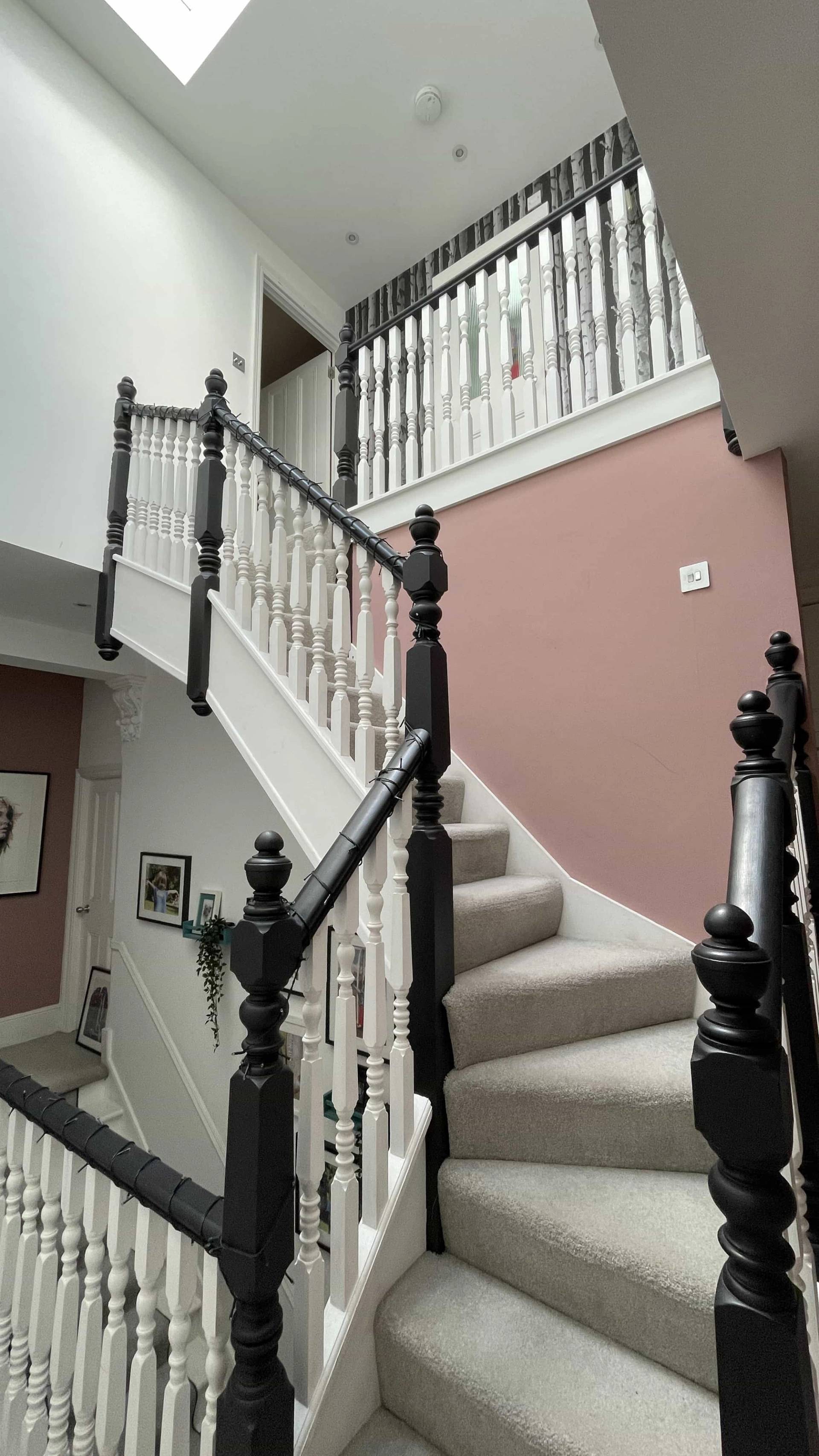High-angle view of a period staircase with black banisters set against plaster pink walls, Love Locations W3.