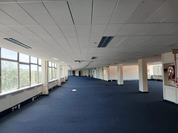 Vast, empty open-plan office film location in Watford WD18 available through Love Locations, featuring blue carpets, a low ceiling, and a long curved wall of windows.