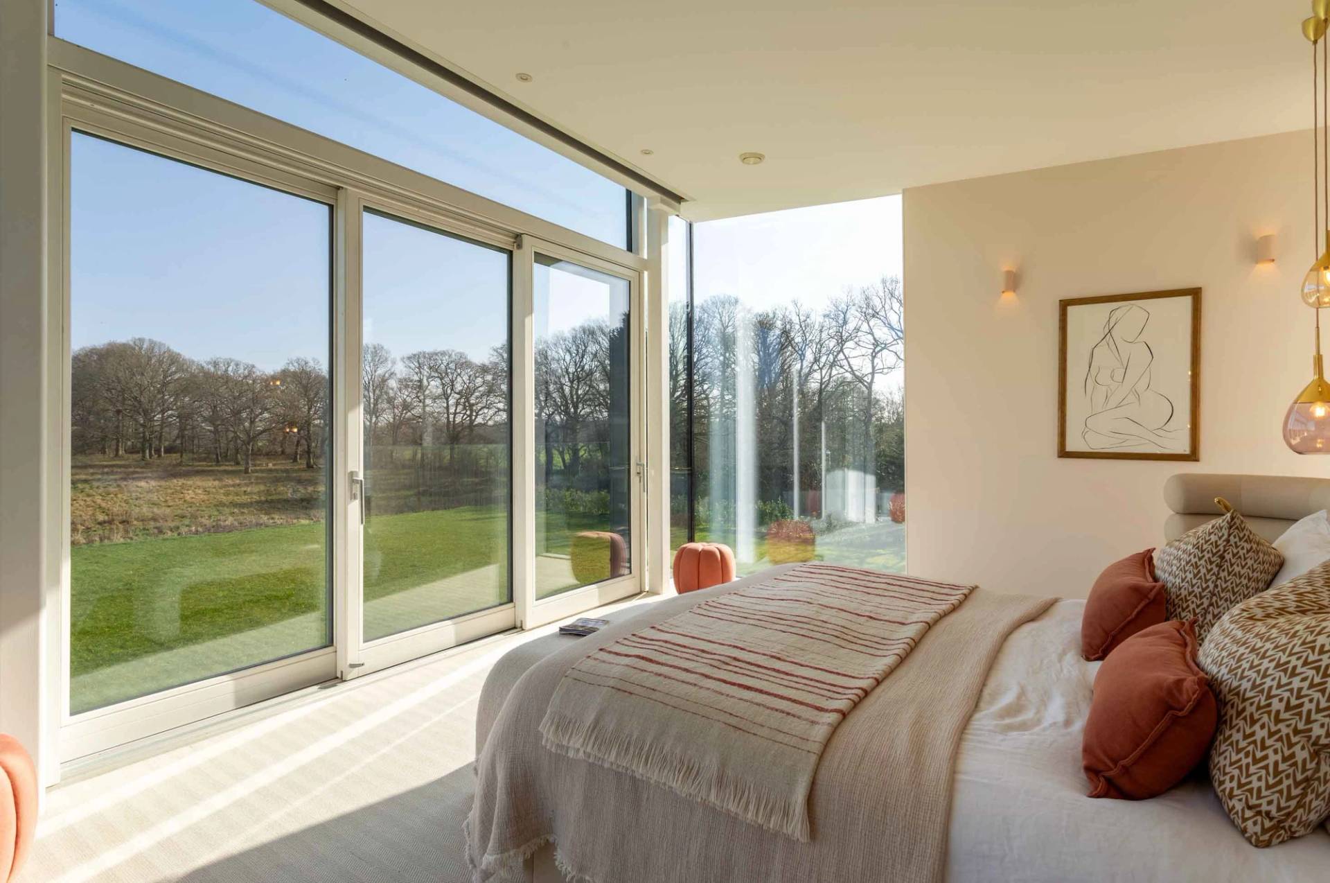 Love Locations daylight bedroom location GU8: Master double bed looking directly through expansive glass architectural panels onto a green lawn, perfect for lifestyle film and TV.
