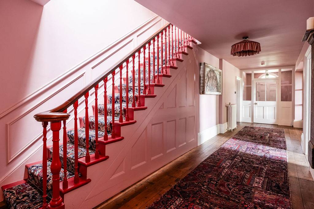 Grand period hallway film location in Liss Hampshire GU33 available via Love Locations, featuring a majestic pink-painted wooden staircase with red railings.