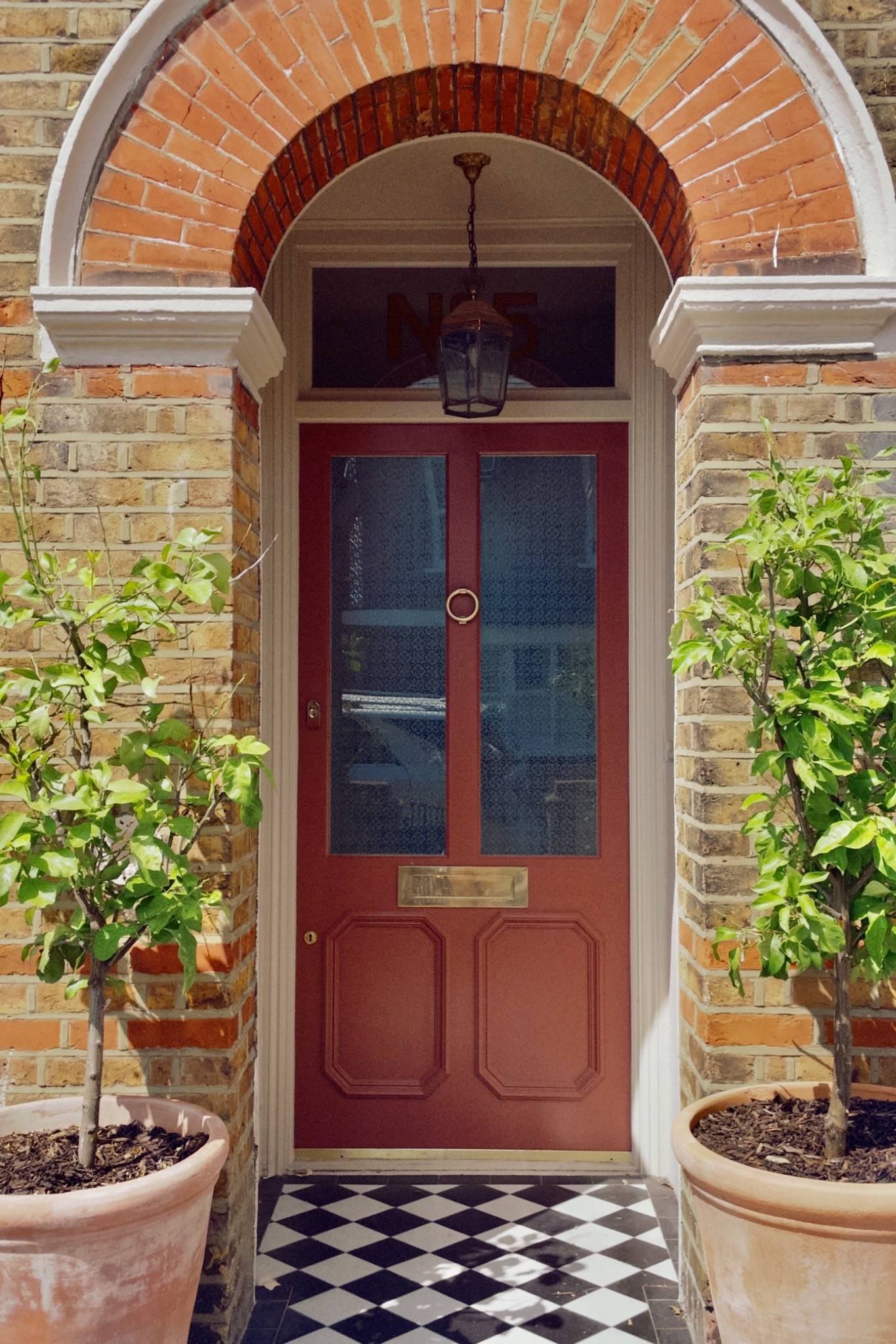 Inviting traditional front entrance exterior featuring a deep red double door, brass hardware, and potted green trees outside a London brick townhouse in Isleworth, TW7, the ultimate exterior welcoming shot for film and TV productions via Love Locations.
