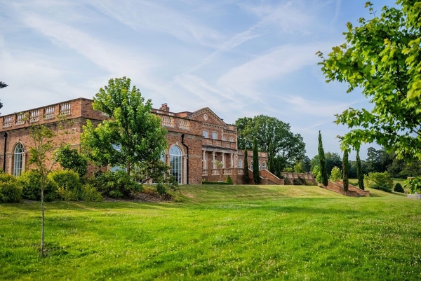 Sweeping green lawns flanking the classic brick architecture of the Greentrees manor house, listed on Love Locations, Haywards Heath.