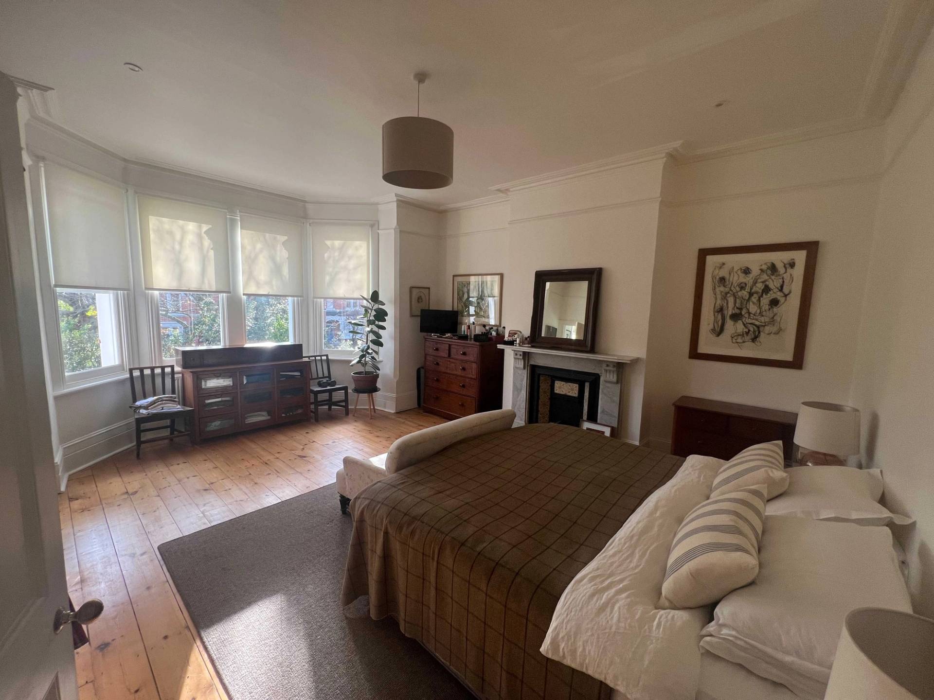 Master bedroom location in Denmark Hill, SE5 featuring a bay window, period fireplace hearth, dark wood furniture, and stripped floorboards, Love Locations.