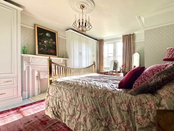 Light-filled bedroom featuring a brass bed, marble fireplace surround, and pink drapery, Love Locations N13.