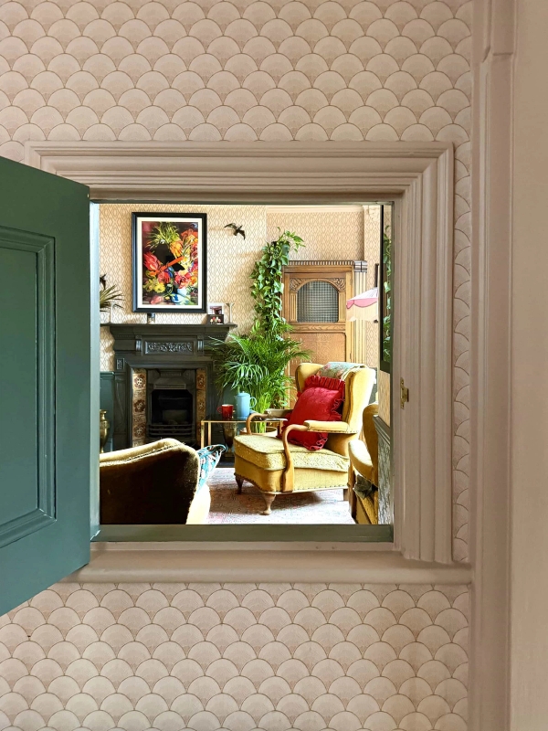 Framed doorway perspective looking into a period living room with mustard yellow armchair and fireplace, Love Locations N13.