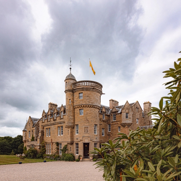 Turreted Scottish castle exterior view framed by estate greenery under dramatic skies in Fife, Love Locations KY15.