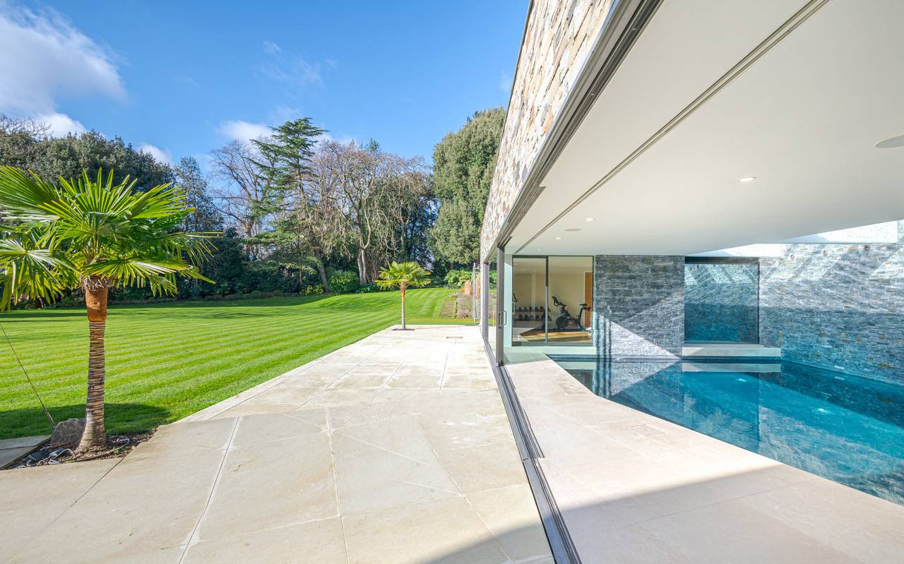 Architectural stone terrace patio opening into an indoor swimming pool suite via glass sliding doors, Love Locations KT2.