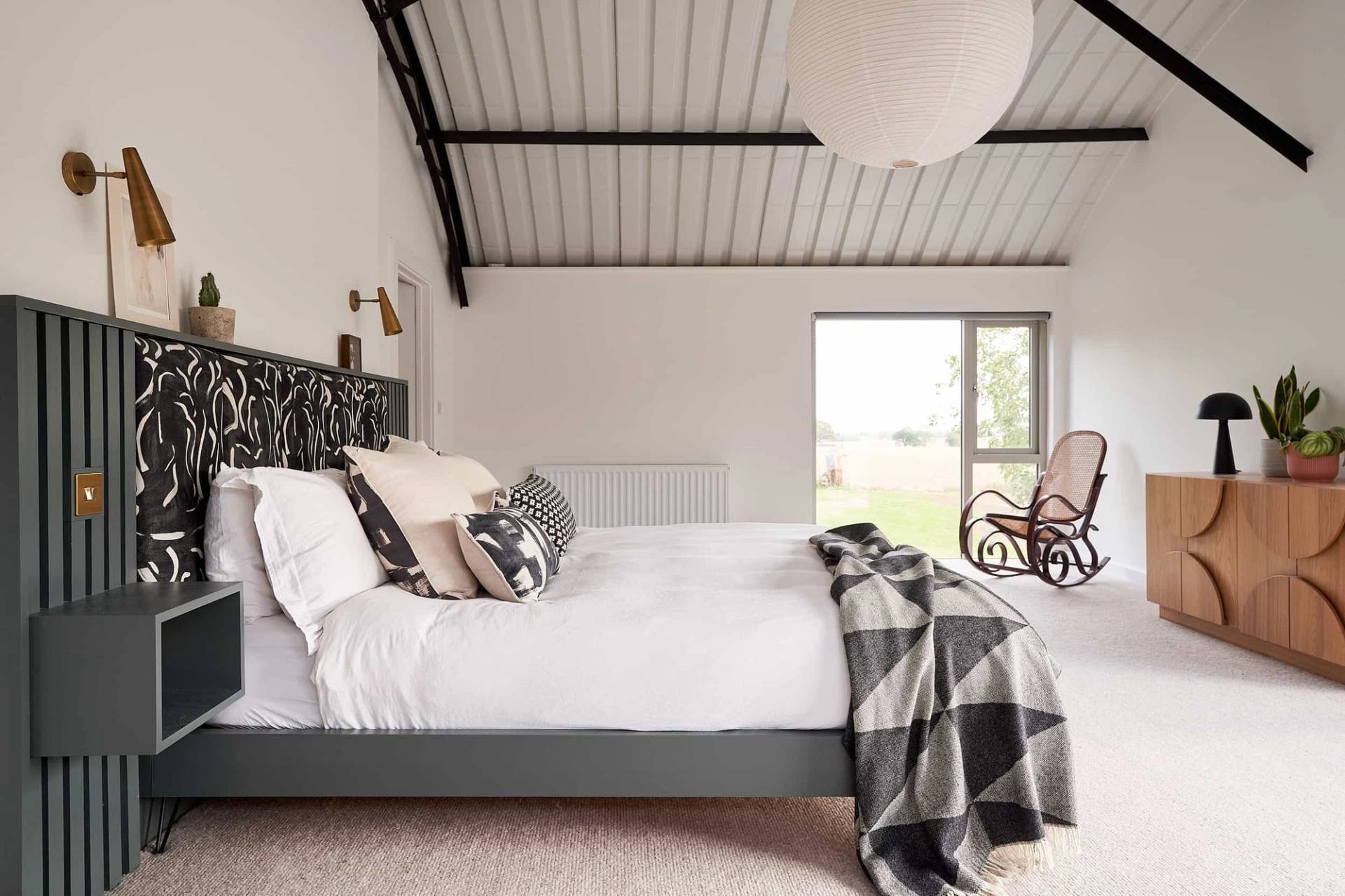 Light-filled master bedroom with corrugated steel ceiling, white linen, and rocking chair, Love Locations IP30.
