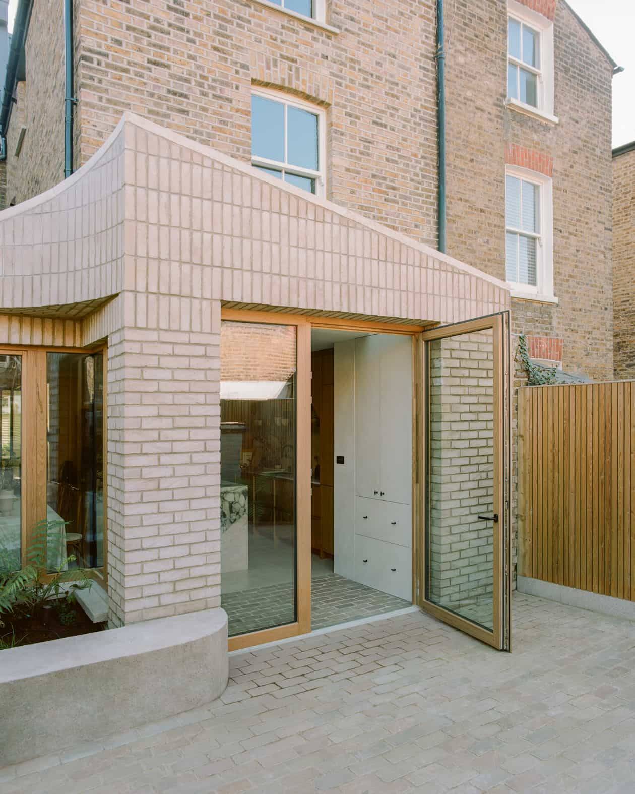Architectural pale brick rear extension facade opening via oak-framed double doors onto a stone garden patio, Love Locations SW4.