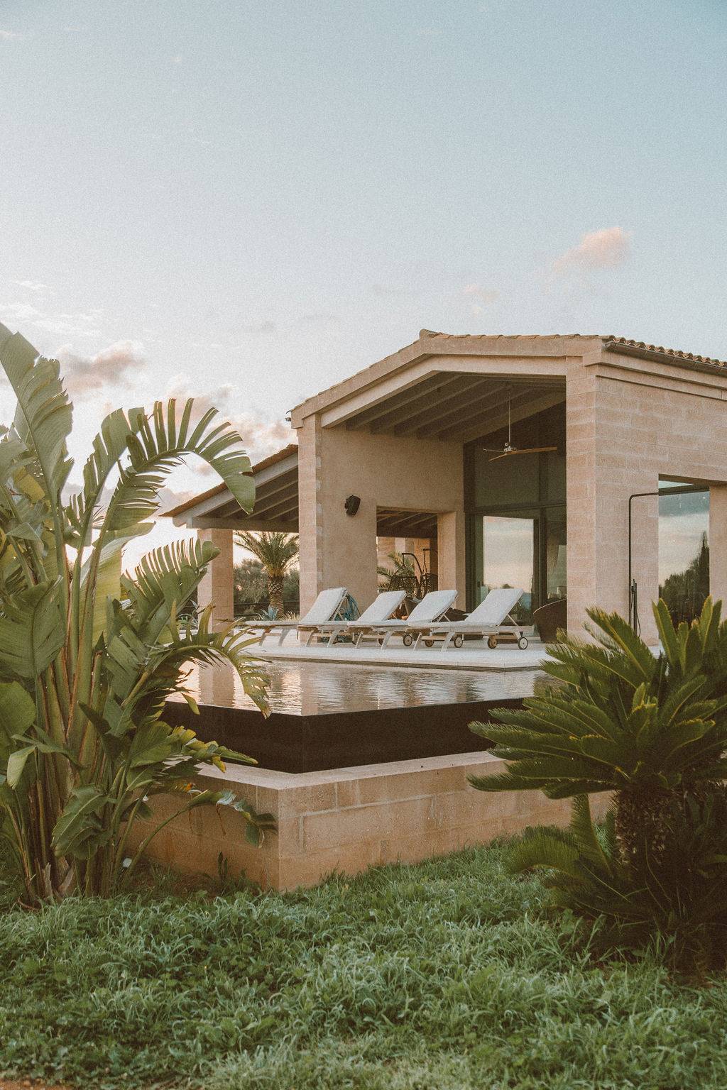 Modern villa exterior architecture featuring an elevated pool terrace, stone walls, and palm landscaping, Love Locations 07630.