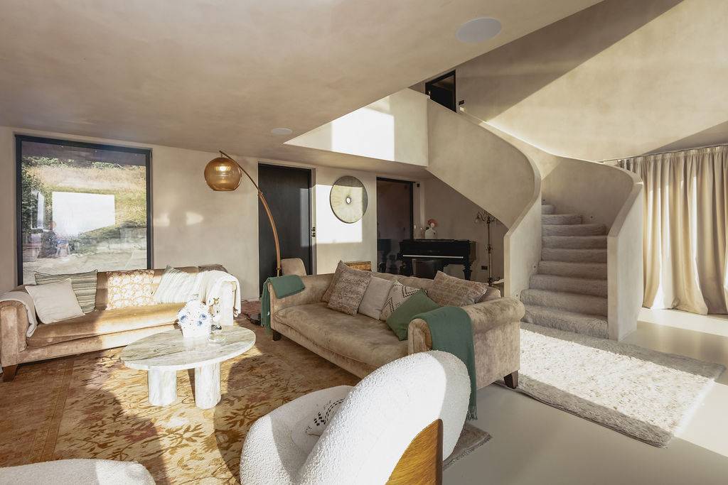 Open-plan living space with cream microcement plaster walls, curved staircase, beige sofas, and round coffee table in Petersfield, Love Locations GU32.
