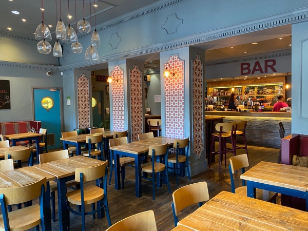 Light-filled cafe seating area with light wood tables, blue wooden chairs, and soft blue painted walls at The Ritzy Cafe in Brixton SW2 via Love Locations.