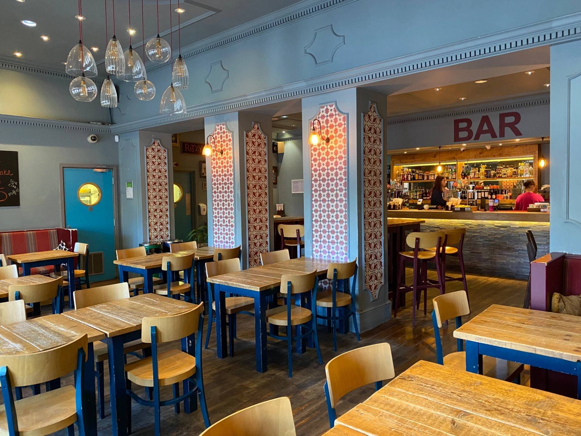 Light-filled cafe seating area with light wood tables, blue wooden chairs, and soft blue painted walls at The Ritzy Cafe in Brixton SW2 via Love Locations.
