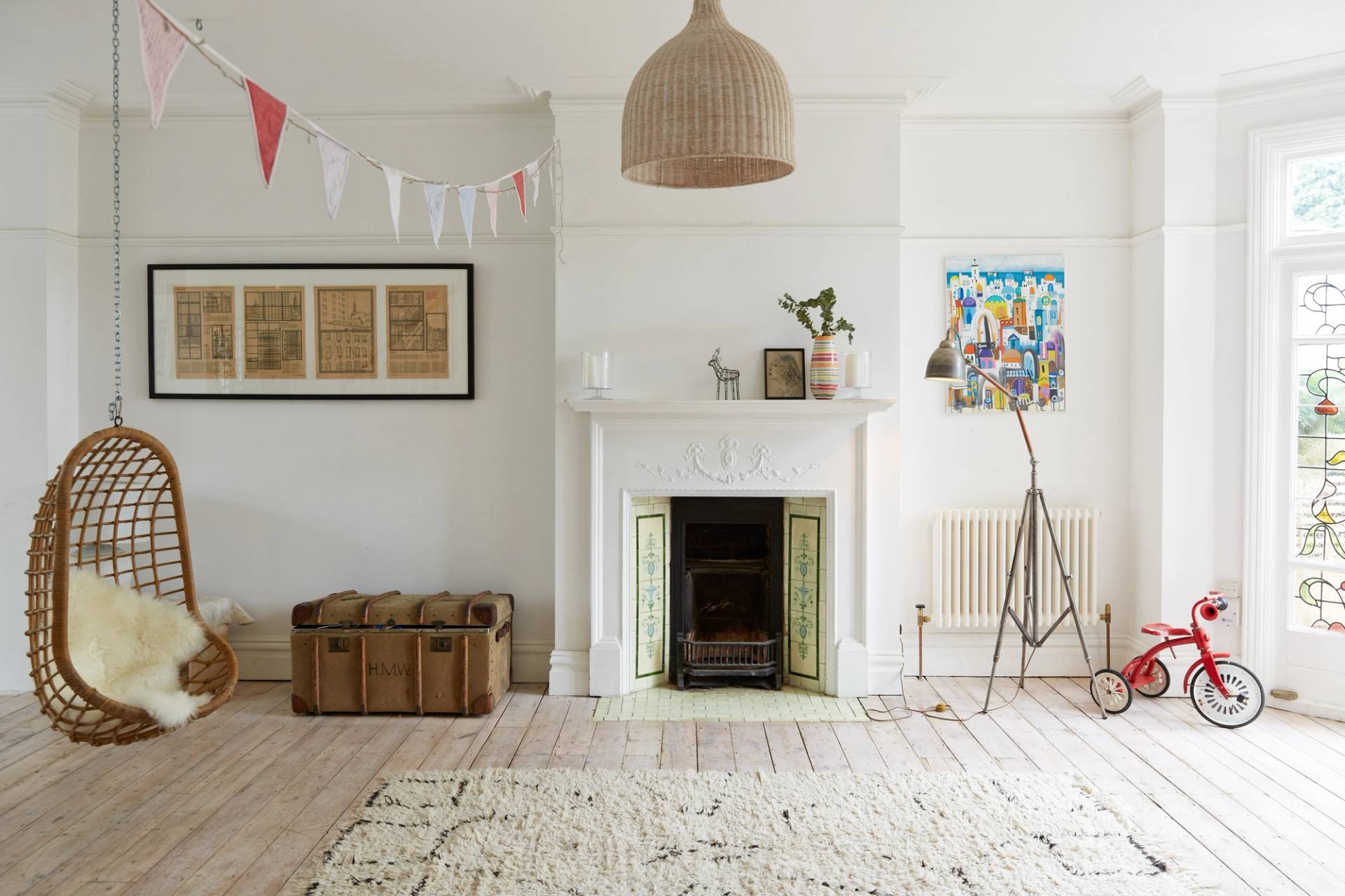 Neutral reception room featuring a white period fireplace hearth, vintage storage chest, Berber rug, and bunting decor, Love Locations N13.