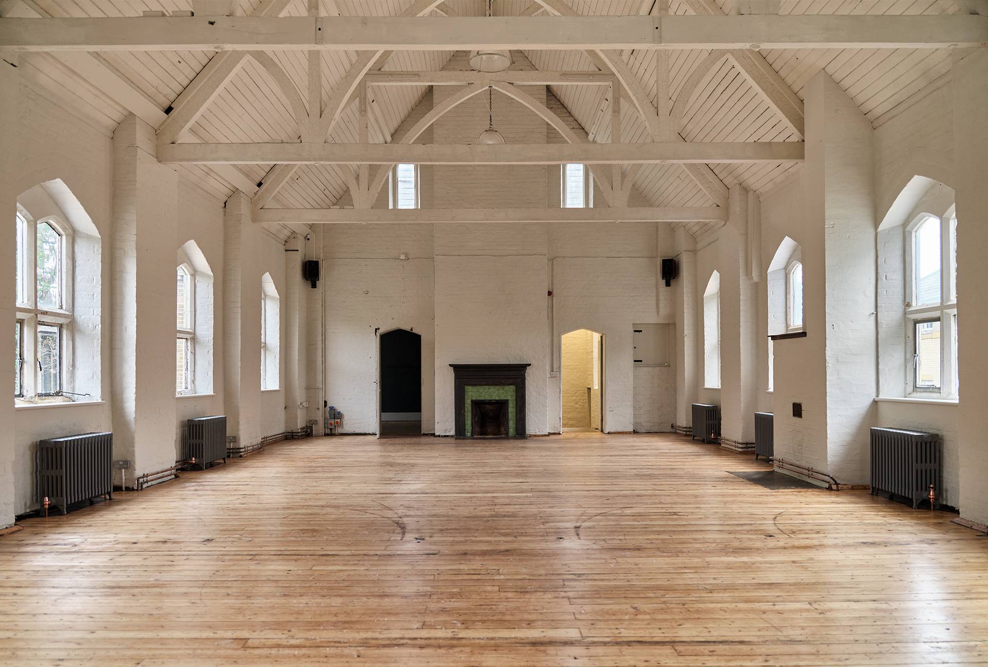 Empty white hall venue with white painted roof trusses and dark fireplaces, ideal for creative set builds and art installations, Love Locations.
